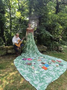 Marianne porte une grande robe verte et à ses cotés, un musicien joue de la guitare