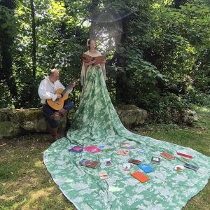 Marianne porte une grande robe verte et à ses cotés, un musicien joue de la guitare